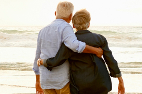 Retired couple standing arm in arm facing the ocean