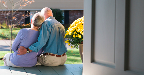 Retired couple hugging on the front porch of their house