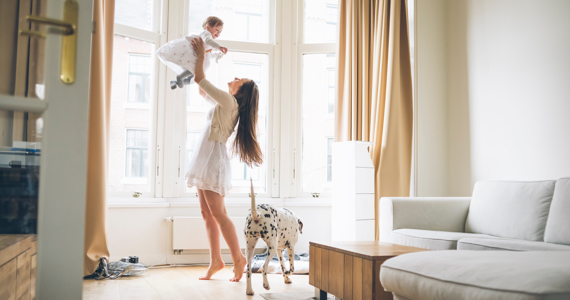 Happy woman raises her baby in the air in her living room