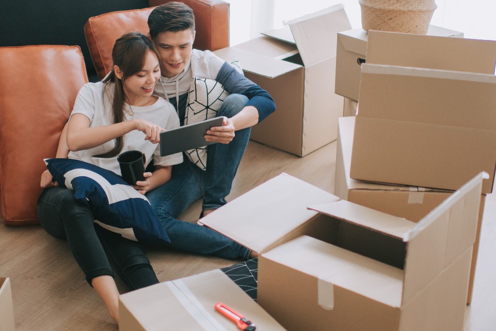A young couple prepares their move surrounded by cardboard boxes in their bright living room.