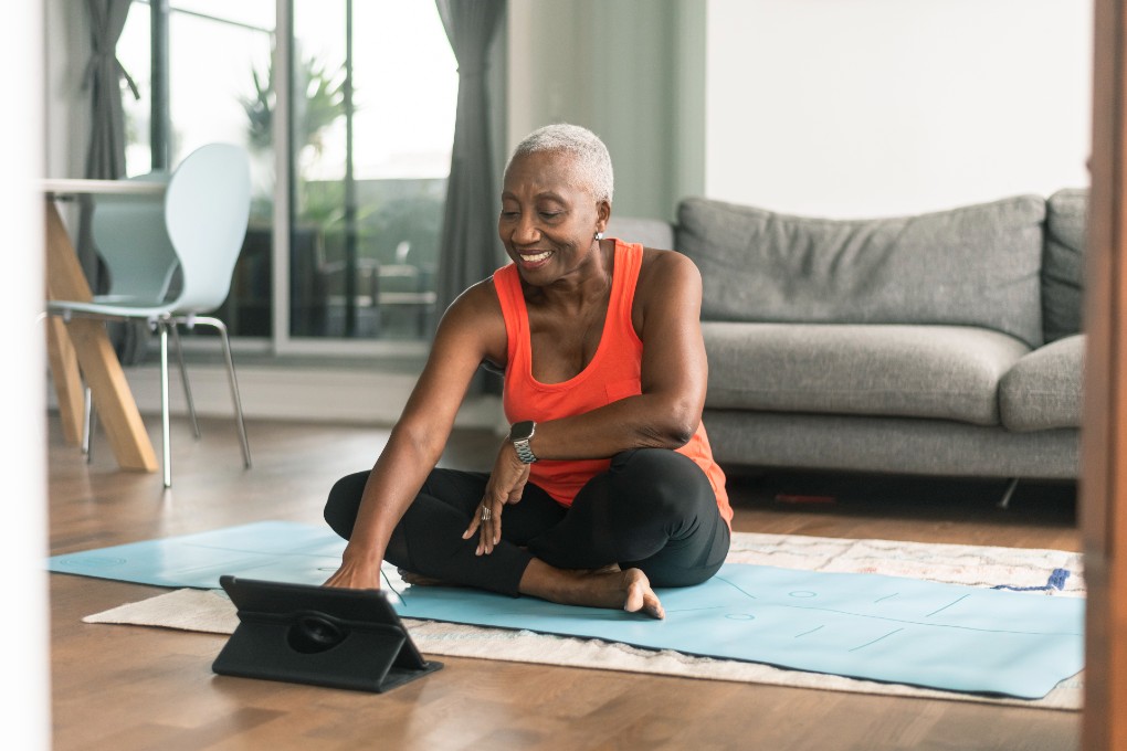 woman-yoga-tablet-retirement A retired woman, sitting on the floor, is about to do some yoga, with her tablet.