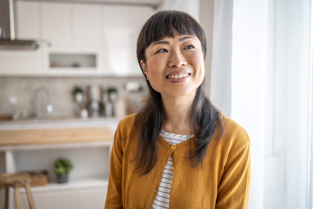 A woman is in her home, smiling and she is smiling and thinking about her early retirement.