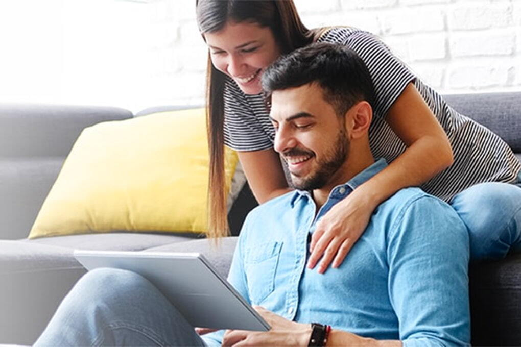 Photo of an happy couple sitting on a sofa and looking at a tablet