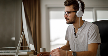 Image of a man sitting at his desk wearing earphones