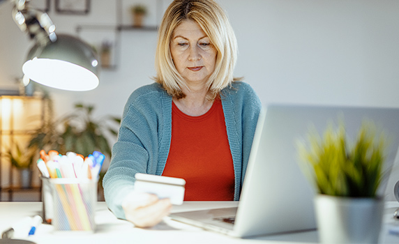 Photo of a woman looking at her credit card in front of her laptop computer