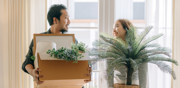 Photo d’un homme transportant une boîte et d’une femme transportant une plante dans une nouvelle maison