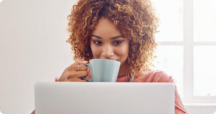 Photo of a woman drinking coffee while working on their laptop